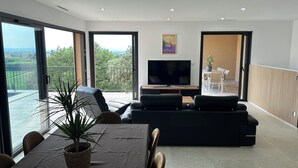 Un salon moderne doté d’un grand téléviseur, de sièges confortables, d’un coin repas et d’un balcon offrant une vue panoramique.