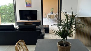 Un salon moderne comprenant un canapé, un téléviseur, une table à manger et un balcon offrant une vue sur la verdure.