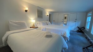 Una camera d'albergo con due letti, un comodino, una lampada a parete, una porta e una finestra.