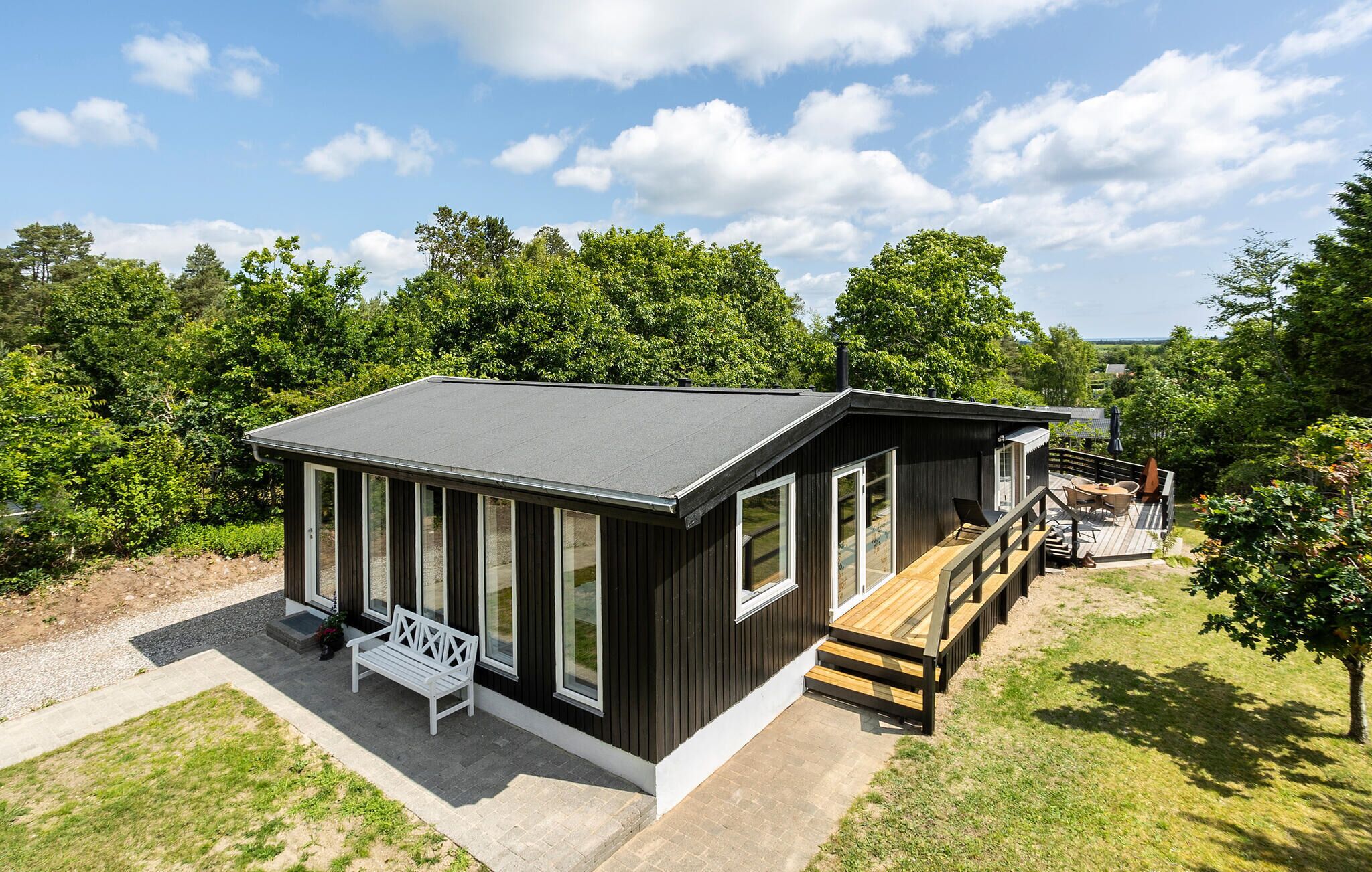 En moderne hytte med terrasse, store vinduer og græsplæne.