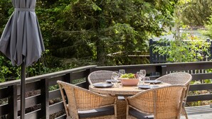 An outdoor dining area with wicker chairs and a round table set for two, surrounded by greenery. - Beautiful Home In Ebeltoft With Sauna (Ebeltoft)