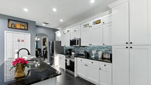 A modern kitchen with white cabinets, a black countertop, and stainless steel appliances. - 5 Bedroom Pool Home in Gated Community Near Disney (Kissimmee)