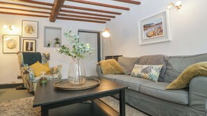 A living room with a grey sofa, a patterned armchair, a coffee table, and a vase with green plants. - Elm Cottage (Moreton-in-Marsh)