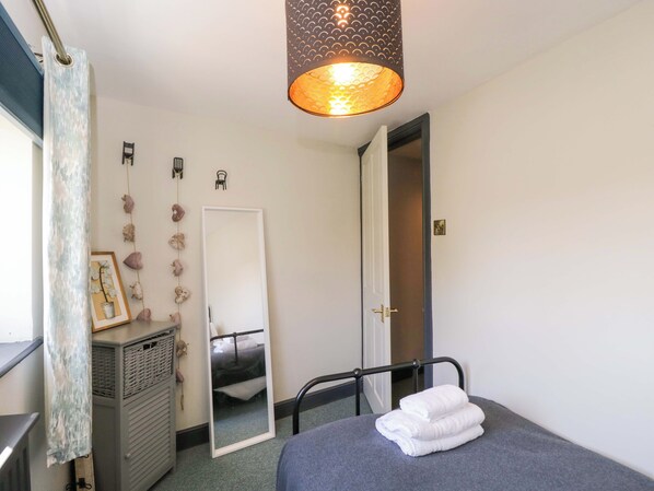 A bedroom with a bed, a mirror, a hanging light fixture, and a door. - Elm Cottage (Moreton-in-Marsh)