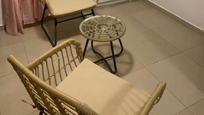 A room with a wicker chair and a small round table, a white door with frosted glass panels, and a telephone mounted on the wall. - Casa de nonoiluzia (Tarrafal)