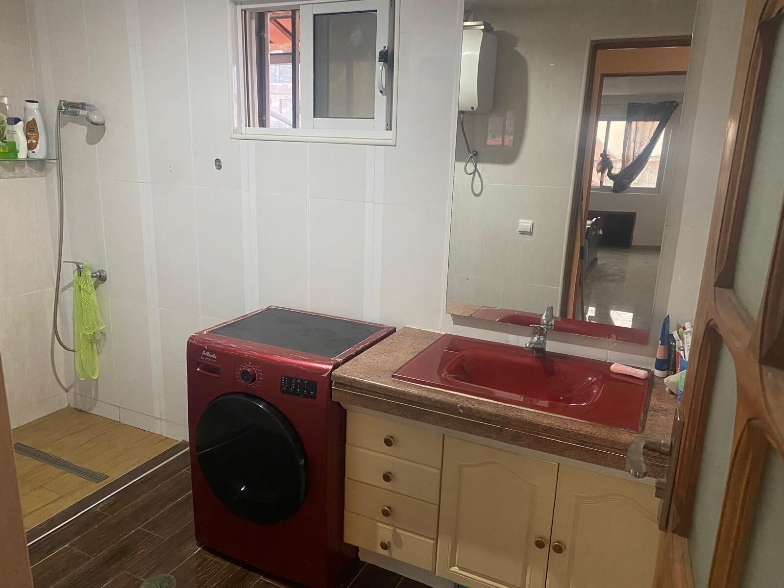 Un baño pequeño con lavadora roja, un lavamanos con espejo y un ventanal.