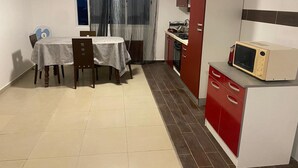 A compact kitchen with a dining table and chairs, a microwave, and a stove. - Casa de nonoiluzia (Tarrafal)