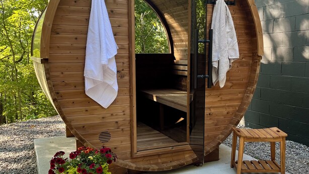 Una sauna de madera con techo curvo, un banco en su interior y dos toallas colgadas en la puerta.
