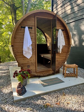 Un sauna en bois doté d’un toit incurvé, d’un banc à l’intérieur et de deux serviettes accrochées à la porte.