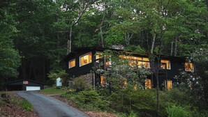 Una cabaña con garaje y un cobertizo pequeño, rodeada de bosque denso.