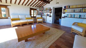 A cozy living room with wicker furniture, a wooden coffee table, and a bookshelf filled with books.