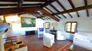 A rustic room with exposed wooden beams, white furniture, a large painting, and a patterned rug.
