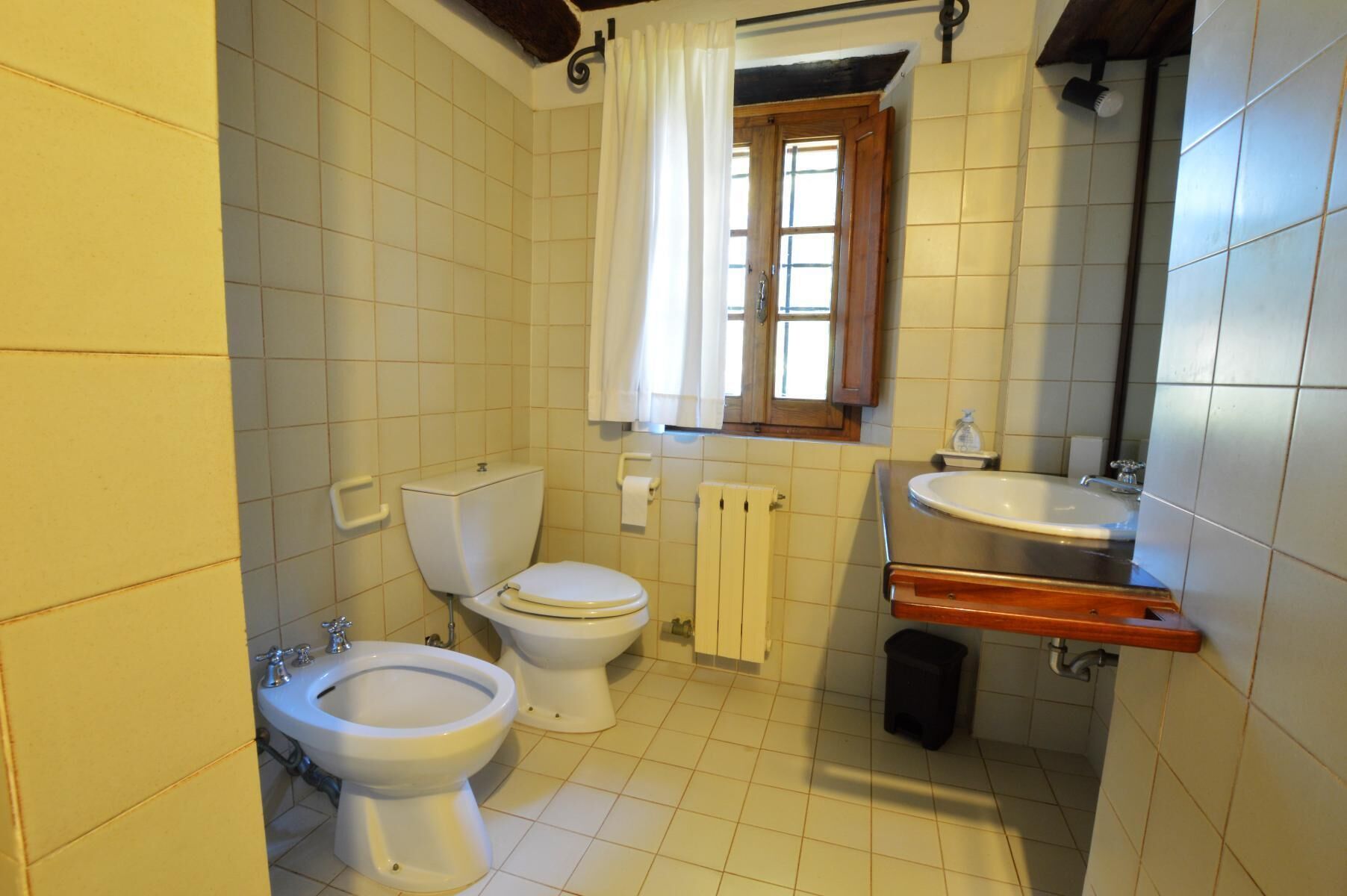 Ein Badezimmer mit zwei Toiletten, einem Bidet, einem Waschbecken und einem Fenster mit Vorhängen.