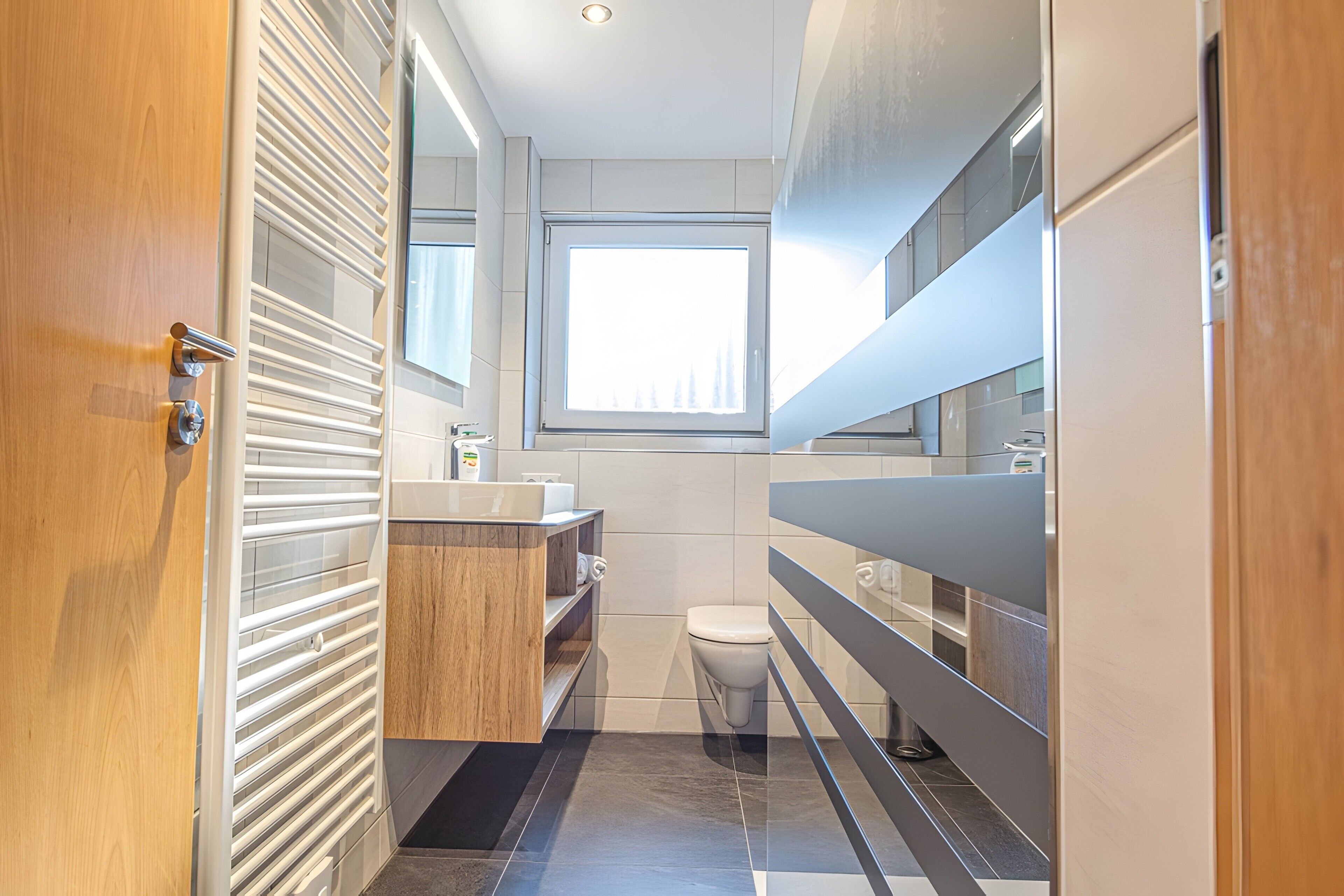 Une salle de bain moderne avec une porte en bois, une fenêtre, des toilettes et un lavabo.