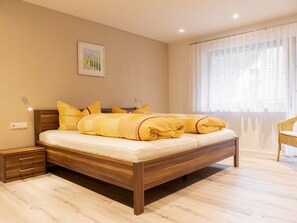 Un dormitorio con una cama de madera, una mesita de noche, una silla y una ventana con cortinas de encaje.