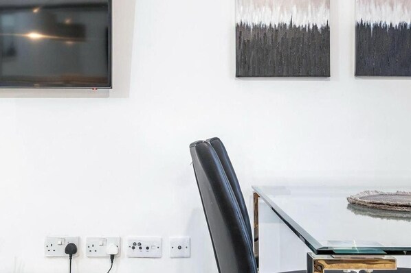 A modern room with a glass table, a black leather chair, and three paintings on the wall. - Luxury Central London Balcony 1-bed Apt w/ Parking (London)