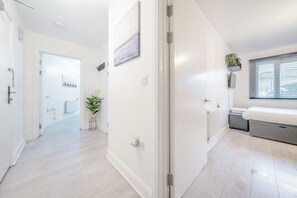 A modern hotel room with a bed, a radiator, a window with blinds, a plant, and a door leading to another room. - Luxury Central London Balcony 1-bed Apt w/ Parking (London)