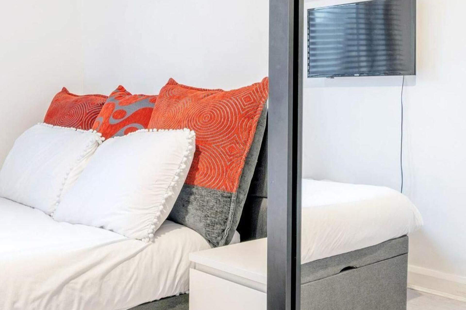 Un dormitorio con una cama, dos almohadas, una mesita de noche y un televisor montado en la pared.