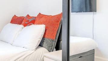A bedroom with a bed, two pillows, a bedside table, and a TV mounted on the wall.