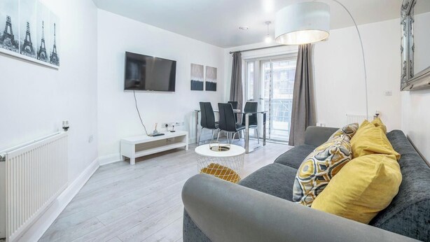 En moderne stue med en grå sofa, et hvidt tv-møbel, et spiseområde med stole og et stort vindue med gardiner.