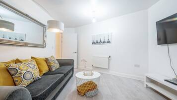 A modern living room with a grey sofa, a round coffee table, and a flat-screen TV mounted on the wall.