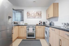 A modern kitchen with stainless steel appliances, wooden cabinets, a large window with blinds, and a cityscape artwork on the wall. - Luxury Central London Balcony 1-bed Apt w/ Parking (London)