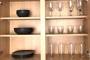 A wooden cabinet with shelves holding black bowls, wine glasses, and clear drinking glasses. - Luxury Central London Balcony 1-bed Apt w/ Parking (London)