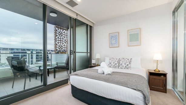 A modern hotel room with a large bed, a balcony with a chair, and two framed artworks on the wall. - Convenient City Apartment in the Heart of Braddon (Braddon)