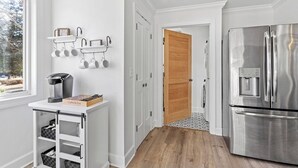 A modern kitchen with white cabinetry, a stainless steel refrigerator, and a coffee station with mugs and a coffee maker. - Relax In Raleigh - Room for Friends & Family! (Raleigh)
