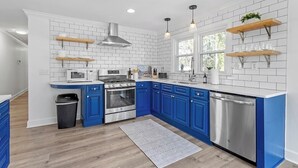 A modern kitchen with blue cabinets, white subway tiles, stainless steel appliances, and wooden shelves. - Relax In Raleigh - Room for Friends & Family! (Raleigh)