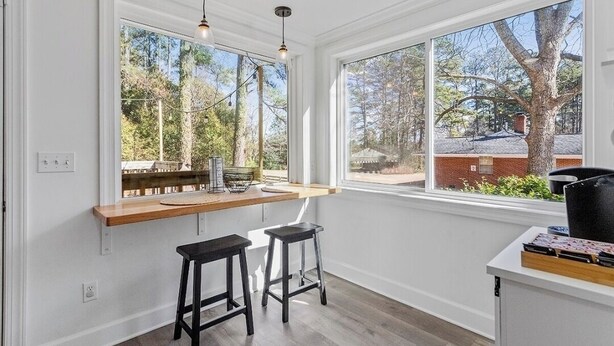 A bright room with large windows, a wooden bench, two black stools, and a small table with a basket and a lamp. - Relax In Raleigh - Room for Friends & Family! (Raleigh)