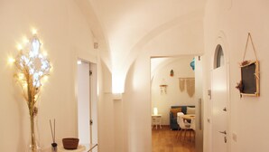 A hallway with a staircase leading to a dining area. There is a vase with dried flowers on a table, a small basket, and a wall-mounted shelf with a picture frame. - Charming abode in the heart of Monopoli, spacious, cozy, close to everything. (Monopoli)