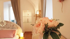 A bedroom with a bed, a bedside table with a candle, and a floral arrangement on the wall. - Charming abode in the heart of Monopoli, spacious, cozy, close to everything. (Monopoli)