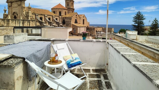 A rooftop terrace with a white lounge chair, a small round table with drinks, and a view of a historic church and the sea. - Charming abode in the heart of Monopoli, spacious, cozy, close to everything. (Monopoli)