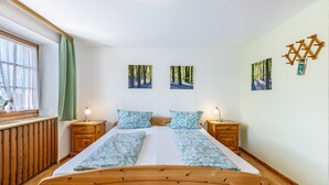 Ein Schlafzimmer mit einem hölzernen Bett, zwei Nachttischen, einem Fenster mit Vorhängen und an der Wand befestigten Bildern.