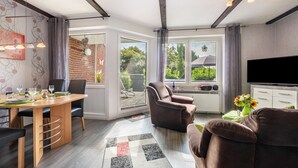 Een moderne woonkamer met een eethoek, een flatscreen televisie en een groot raam met uitzicht op de omgeving.