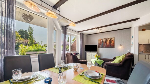 Een eethoek met een tafel voor vier personen, een bank, een televisie en een keuken op de achtergrond.