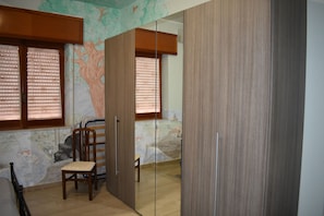 A room with a wooden wardrobe, a chair, and a bed.