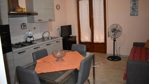 Una cocina compacta con una mesa de comedor, sillas, cafetera y ventilador.