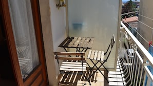 Un balcón con mesa y sillas de madera, vistas a la ciudad y una ventana con cortina.
