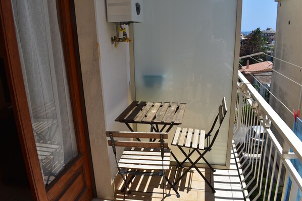 A balcony with a wooden table and chairs, a view of the city, and a window with a curtain.