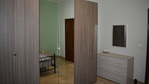 Un dormitorio con armario, cómoda, espejo y cama con estructura metálica.