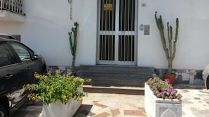 Un edificio con entrada protegida por una reja, plantas en macetas y un coche estacionado.
