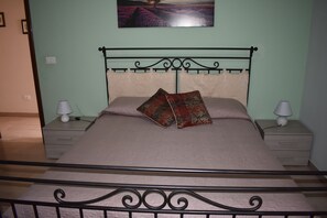 A neatly made bed with a metal frame, two bedside tables with lamps, and a wall-mounted picture. - Naxos nature apartments (Giardini Naxos)