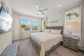 A bedroom with a bed, bedside table, bench, ceiling fan, and large windows.