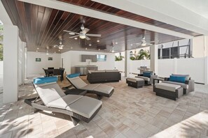 An outdoor patio area with wicker furniture, ceiling fans, and a kitchen in the background.