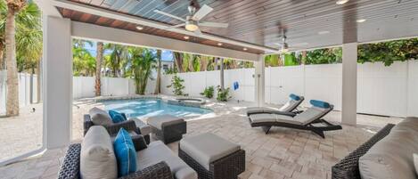 A covered outdoor area with a pool, lounge chairs, and wicker furniture.