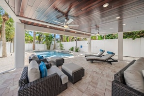 A covered outdoor area with a pool, lounge chairs, and wicker furniture.