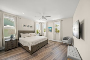 A bedroom with a bed, bedside tables, a chair, a ceiling fan, and artwork on the walls.