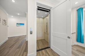 A modern interior with a wooden floor, a door leading to a room with a light-colored wall, and a window with a blue curtain. - Luxury 6 Bedroom near the Village (Siesta Key)